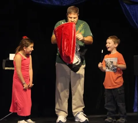 Magician Ed Popielarczyk performs a magic trick with two young children. 