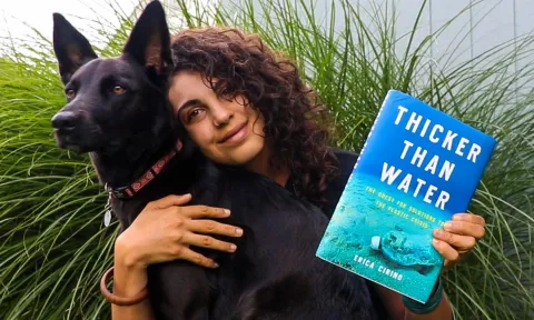 A photo of the Author Erica Cirino holding her book "Thicker Than Water" and a dog.