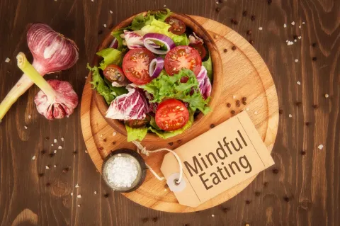 A salad in a wooden bowl with a sign that says "mindful eating"