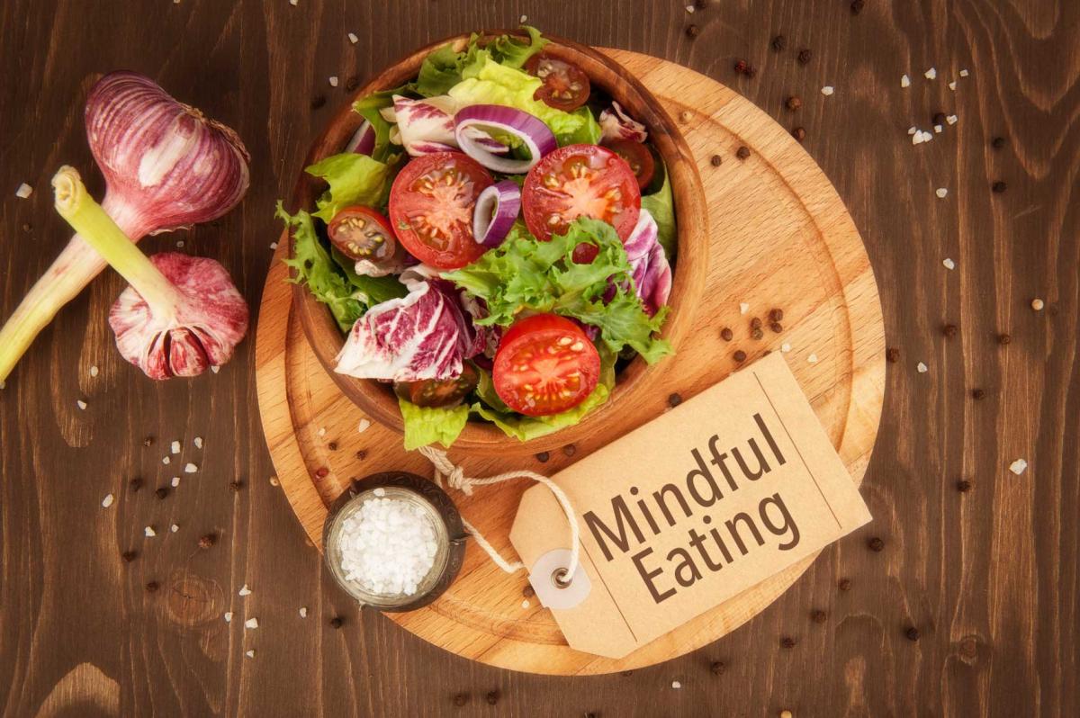 A salad in a wooden bowl with a sign that says "mindful eating"
