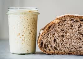 A picture of a jar of sourdough starter next to a loaf of sourdough bread. 